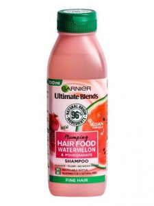 A short rectangular White Plastic Bottle with a bright green lid and a bright green label that has Garnier Ultimate Blends Hair Food Watermelon Shampoo written in bold black writing and a picture of a Watermelon on it, on a white background. 