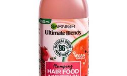 A short rectangular White Plastic Bottle with a bright green lid and a bright green label that has Garnier Ultimate Blends Hair Food Watermelon Shampoo written in bold black writing and a picture of a Watermelon on it, on a white background.