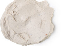 A medium circular puddle of creamy white face mask that has some pieces of dried dates running through it, on a white background.