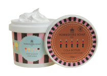 A short cylindrical white plastic tub with a pink and black striped label that has The Yorkshire Soap Company Cola Bottles Soap & Sugar Whip Scrub written in dark blue writing and some pictures of some bright white ice creams on it, on a white background.
