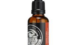 A short cylindrical brown glass bottle with a black rubber pipette lid and a white label that has Arthur J Hawke Jaffa Cake Beard Oil written in bold white writing and a picture of a black and white hawk on it, on a white background.