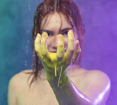 A tall woman that has some bright yellow shower slime dripping through her hands, on a white background.