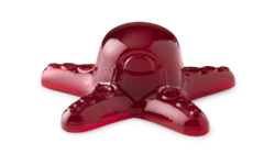 A large dark red octopus shaped block of shower jelly that has a red Eye and some red suckers on it, on a white background.
