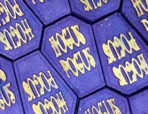 A large deep purple coffin shaped Bath Bomb that has Hocus Pocus written in bold white writing on it, on a white background.