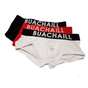 A pair of black, red and white folded up boxers with a black waistband that has Buachaill written in bold white writing on it, on a white background.
