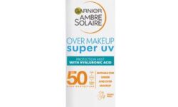 A tall cylindrical Metallic White Aerosol Can with a white plastic lid that has Garnier written in bright blue writing, Ambre Solaire Over Makeup Super UV Protection Mist written in bold black writing, and SPF50 written in bold gold writing on it, on a white background.