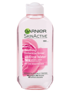 A tall rounded rectangular pale pink plastic bottle with a white Plastic lid that has Garnier Naturals Rose Water Toner For Sensitive Skin written in bold black writing and a picture of a large bright pink rose on it, on a white background.