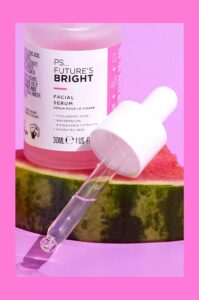 A short cylindrical clear glass bottle full of some bright pink liquid with a white rubber pipette lid and a white label that has Primark PS Futures Bright Facial Serum written in bold black writing and a picture of a bright pink stripe on it, on a white background.