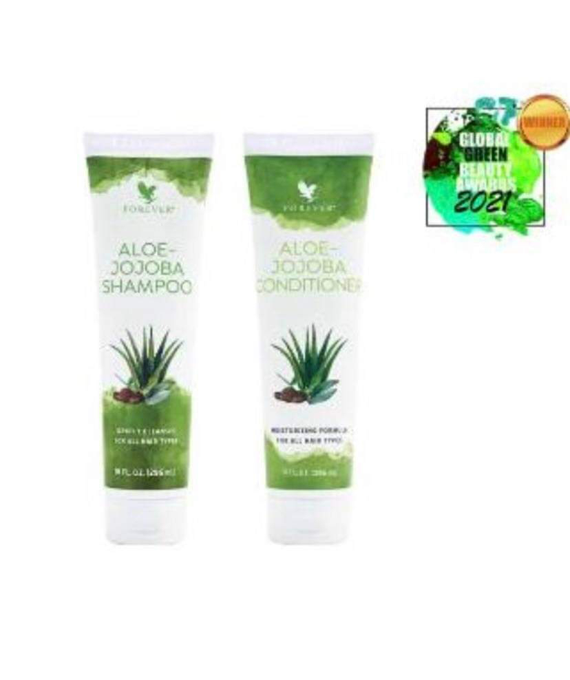 A tall cylindrical White Plastic Bottle with a white plastic lid and a white label that has Forever Living Aloe Jojoba Shampoo written in bright green writing and some pictures of some large dark green aloe vera leaves on it next to a tall cylindrical White Plastic Bottle with a white plastic lid and a white label that has Forever Living Aloe Jojoba Conditioner written in bright green writing and some pictures of some large dark green aloe vera leaves on it, on a white background.