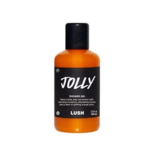 A tall cylindrical clear plastic bottle full of some dark orange liquid with a white label that has Lush Jolly Shower Gel written in bold black writing on it, on a white background.