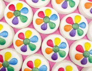 A large circular shaped bright white bath bomb that has a bright pink, yellow, orange, purple, blue, and green flower design engraved on it, on a white background.