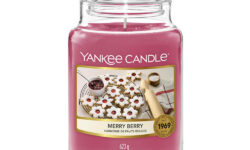 A tall cylindrical Glass Jar full of some bright pink wax with a label that has Yankee Candle written in white writing, Merry Berry written in black writing, and some pictures of some bright white and pink star shaped cookies on it, on a white background.