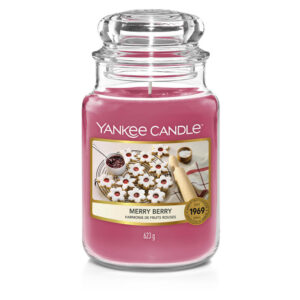 A tall cylindrical Glass Jar full of some bright pink wax with a label that has Yankee Candle written in white writing, Merry Berry written in black writing, and some pictures of some bright white and pink star shaped cookies on it, on a white background.