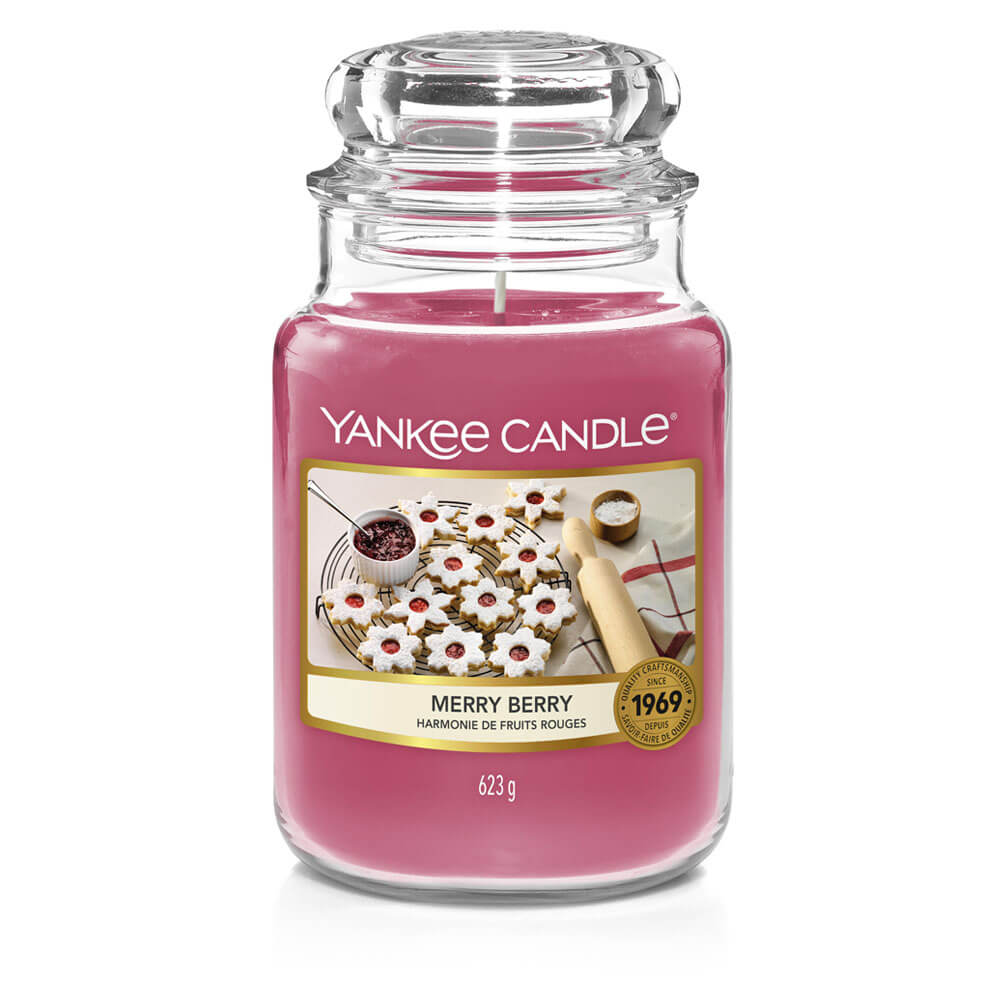 One More Sleep Until It’s Christmas | Yankee Candle Countdown To Christmas Collection A tall cylindrical Glass Jar full of some bright pink wax with a label that has Yankee Candle written in white writing, Merry Berry written in black writing, and some pictures of some bright white and pink star shaped cookies on it, on a white background.