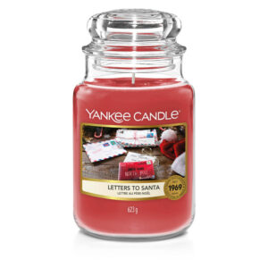 A tall cylindrical glass jar full of some bright red wax with a label that has Yankee Candle written in white writing, letters to Santa written in black writing, and a picture of some pale brown letters and envelopes on it, on a white background.