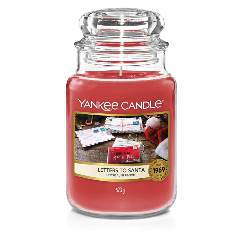 What I Thought of the Yankee Candle Advent House 2014 A tall cylindrical glass jar full of some bright red wax with a label that has Yankee Candle written in white writing, letters to Santa written in black writing, and a picture of some pale brown letters and envelopes on it, on a white background.