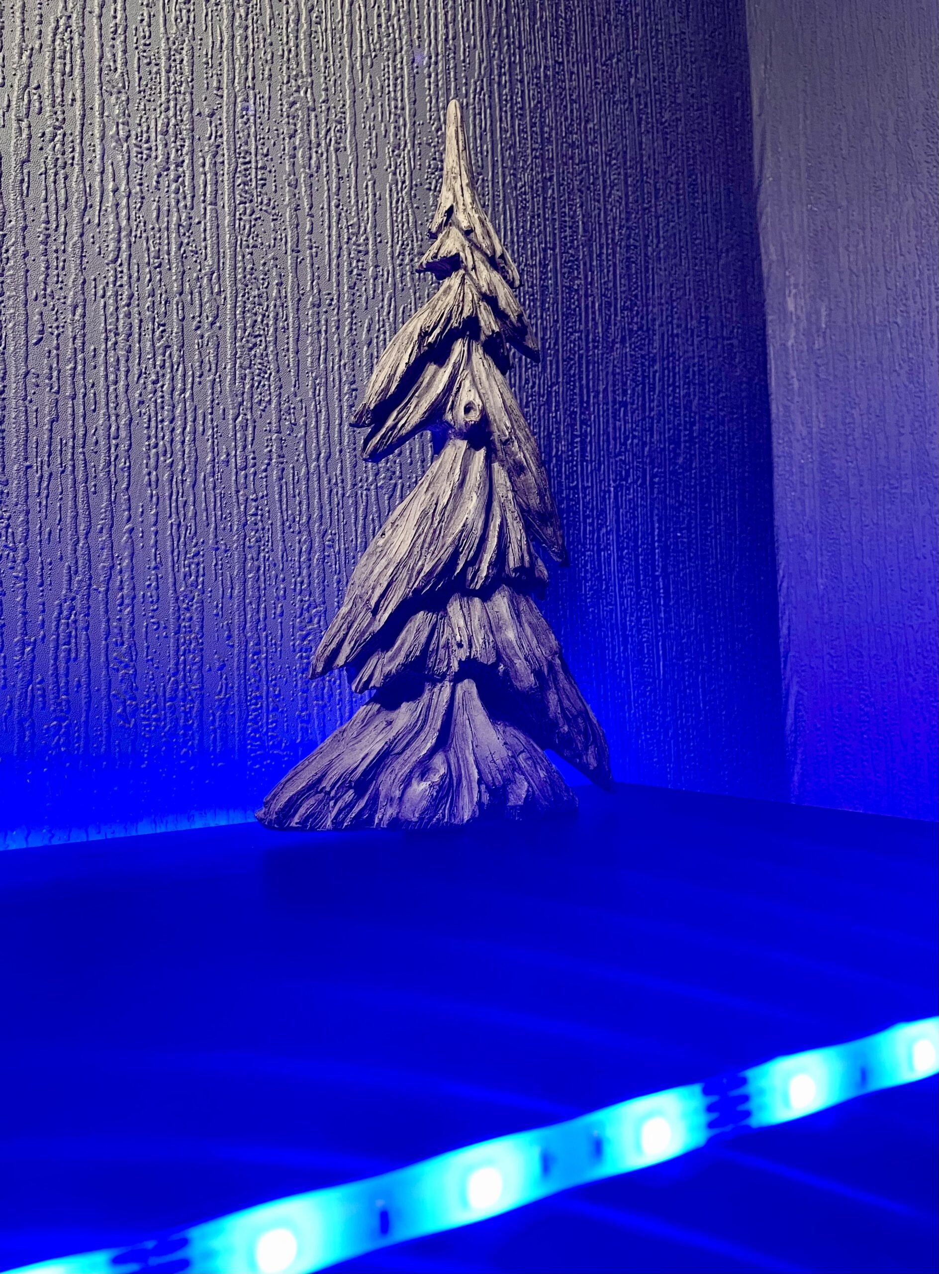 A large triangular bright white and grey resin Christmas Tree, on a black wooden cabinet.