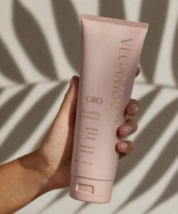 A tall conical bright pink Plastic Tube with a bright pink lid that has Vegamour Grow Revitalising Conditioner written in bold gold writing on it, on a white background.