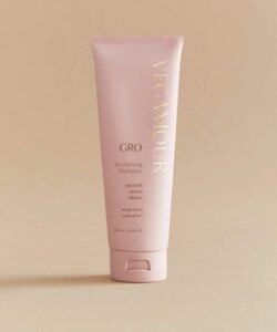 A tall conical bright pink Plastic Tube with a bright pink lid that has Vegamour Grow Revitalising Shampoo written in bold gold writing on it, on a white background.