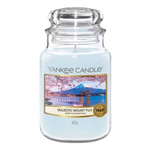 A tall cylindrical glass jar full of some light blue wax with a label that has Yankee Candle written in black writing, majestic mount fuji written in black writing, and some pictures of some light grey mountains on it, on a white background.