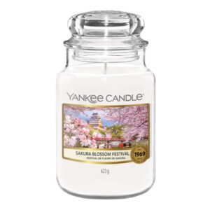 A tall cylindrical glass jar full of some bright white wax with a label that has Yankee Candle written in black writing, Sakura Blossom Festival written in black writing, and some pictures of some pale pink Cherry Blossoms on it, on a white background.