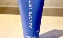 A tall conical bright turquoise plastic tube with a white plastic lid that has Aldi Wonderlust Rescue Mask written in bold white writing on it, on a white background.