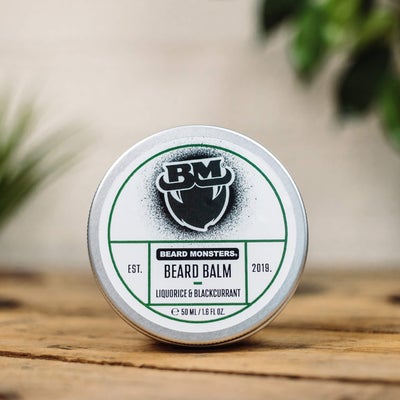 There's A Monster Lurking In The Blackcurrant Bush | Beard Monsters Liquorice & Blackcurrant Beard Balm & Beard Oil Combo A short cylindrical silver metal tin with a white label that has Beard Monsters Liquorice & Blackcurrant Beard Balm written in bold black writing and a picture of a man with a black beard on it, on a white background.