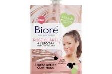 A short rectangular gradient pink and white plastic pouch with a black plastic screw top lid that has Biore Rose Quartz + Charcoal Stress Relief Clay Mask written in bold black writing and a picture of a woman’s face on it, on a white background.