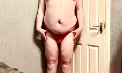 A tall bearded man wearing a pair of bright Red Mesh Briefs with a bright Red Cotton Pouch and a bright White Waistband that has Molly & Tommy written in bold red writing on it stood against a white wooden door.