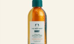 A tall cylindrical metallic Orange Aluminium Bottle with a Silver Aluminium lid and a white label that has The Body Shop Boost Uplifting Hair & Body Wash written in dark green writing and some pictures of some bright Orange swirls on it, on a white background.