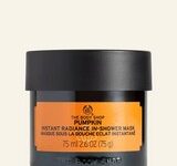 A short cylindrical black glass jar with a black plastic lid and a bright orange label that has The Body Shop Pumpkin Instant Radiance In-Shower Mask written in bold black writing on it, on a white background.
