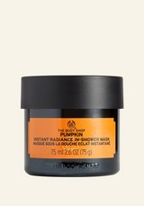 A short cylindrical black glass jar with a black plastic lid and a bright orange label that has The Body Shop Pumpkin Instant Radiance In-Shower Mask written in bold black writing on it, on a white background.