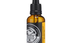 A short cylindrical brown glass bottle with a black rubber pipette lid and a white label that has Arthur J Hawke Sunset Boulevard Beard Oil written in bold white writing and a picture of a black and white hawk on it, on a white background.