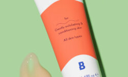 A short bright white plastic tube that has By Beauty Bay 2% BHA Overnight Face Mask with Salicylic Acid and Azelaic Acid written in dark blue writing and a picture of a bright orange stripe on it next to a medium circular puddle of pale orange face mask, on a white background.