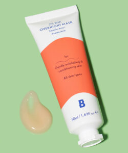 A short bright white plastic tube that has By Beauty Bay 2% BHA Overnight Face Mask with Salicylic Acid and Azelaic Acid written in dark blue writing and a picture of a bright orange stripe on it next to a medium circular puddle of pale orange face mask, on a white background.