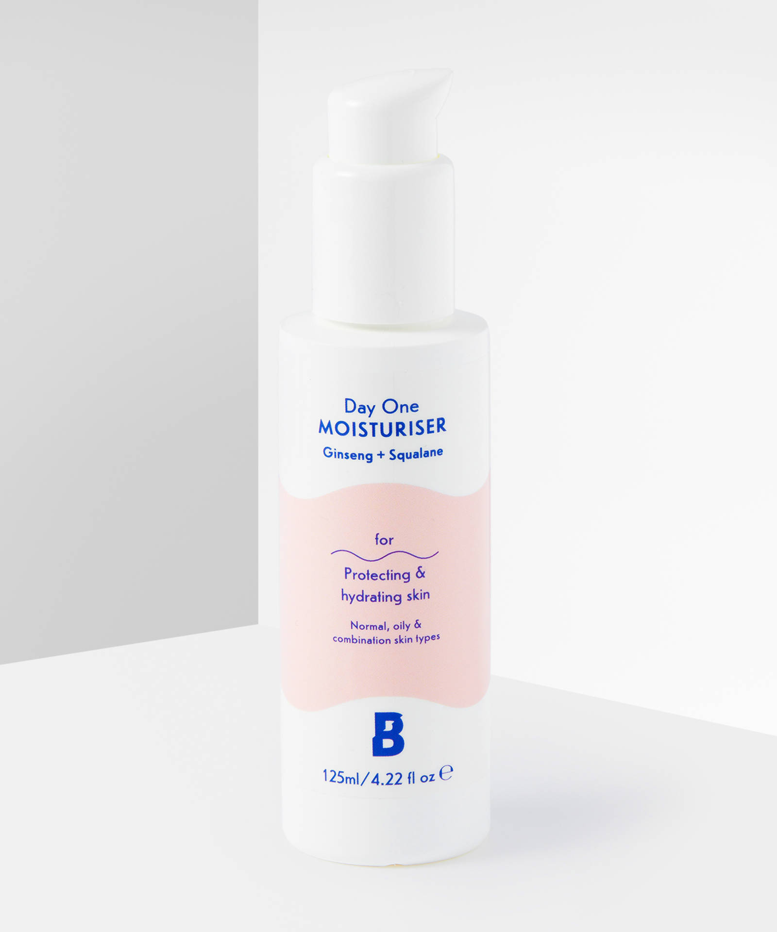 A tall cylindrical white plastic bottle with a white pump lid and a white label that has By Beauty Bay Day One Moisturiser with Ginseng and Squalane written in dark blue writing and a picture of a pale peach stripe on it, on a white background.