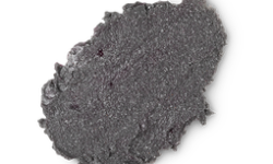 A medium circular puddle of Black Facial Scrub that has some pieces of Castor Sugar running through it, on a white background.