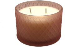 A short cylindrical embossed peach Glass Jar full of some creamy white wax that has two dark brown cotton wicks coming out of the top of it, on a white background.