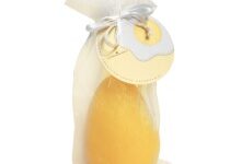 A large bright yellow egg shaped block of soap inside a large bright yellow Organza Bag with a bright yellow label that has The Yorkshire Soap Company Marshmallow & Peach Easter Egg Soap written in bold black writing and a picture of a large fried egg with a bright yellow yolk on it, on a white background.