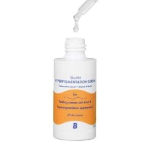 A short cylindrical white plastic bottle with a white rubber pipette lid that has By Beauty Bay SkinHit Hyperpigmentation Serum with Tranexamic Acid and Alpha Arbutin written inn dark blue writing and a picture of a bright orange stripe on it, on a white background.