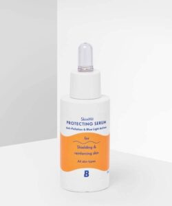 A short cylindrical white plastic bottle with a white rubber pipette lid that has By Beauty Bay SkinHit Protecting Serum with Anti-Pollution and Blue Light Actives written inn dark blue writing and a picture of a bright orange stripe on it, on a white background.