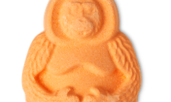 A small bright orange Orangutan shaped Bath Bomb that has it’s arms folded across it’s stomach, on a white background.
