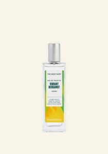 A tall rectangular clear glass bottle full of some clear liquid with a silver aluminium lid and a gradient green and yellow label that has The Body Shop Vibrant Bergamot Eau De Toilette written in dark green writing and some pictures of some bright orange Bergamots on it, on a white background.