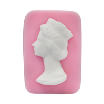 A large rectangular pale pink block of soap that has a picture of a bright white woman wearing a crown engraved on it, on a white background.