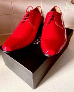 A pair of shiny red patent leather dress shoes with some bright red laces, on a white background.