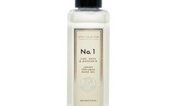 A tall rectangular glass bottle with a black plastic lid and a white label that has Aldi Hotel Collection Lime, Basil & Mandarin Luxury Perfumed Antibacterial Hand Gel written in bold black writing on it, on a white background.