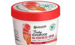 A short cylindrical white plastic tub with a bright red plastic lid that has Garnier Body Superfood written in bright green writing, Watermelon & Hyaluronic Acid written in bright red writing, and a picture of a large oval gradient bright red and orange capsule on it, on a white background.