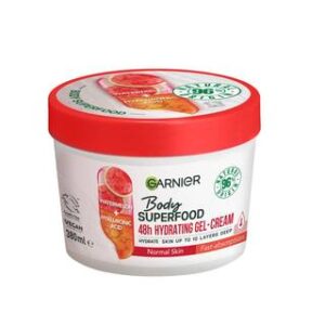 A short cylindrical white plastic tub with a bright red plastic lid that has Garnier Body Superfood written in bright green writing, Watermelon & Hyaluronic Acid written in bright red writing, and a picture of a large oval gradient bright red and orange capsule on it, on a white background.