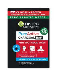 A large rectangular bar of soap wrapped in some black paper that has Garnier written in bold white writing, Pure Active Anti-Spot and Blackhead Solid Wash Charcoal Bar written in bold black writing, and a picture of a Red box on it, on a white background.