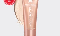 A short cylindrical rose gold Glass Jar with a rose gold lid that has GlamGlow BrightMud™ Dual-Exfoliating Treatment written in bold black writing and a picture of a silver star on it next to a rose gold diamond shaped cardboard box that has GlamGlow BrightMud™ Dual-Exfoliating Treatment written in white writing on it, on a white background.